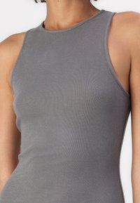 Débardeur gris côtelé avec un design sans manches, un col rond et une texture lisse. Le tissu a une coupe près du corps avec une légère élasticité.