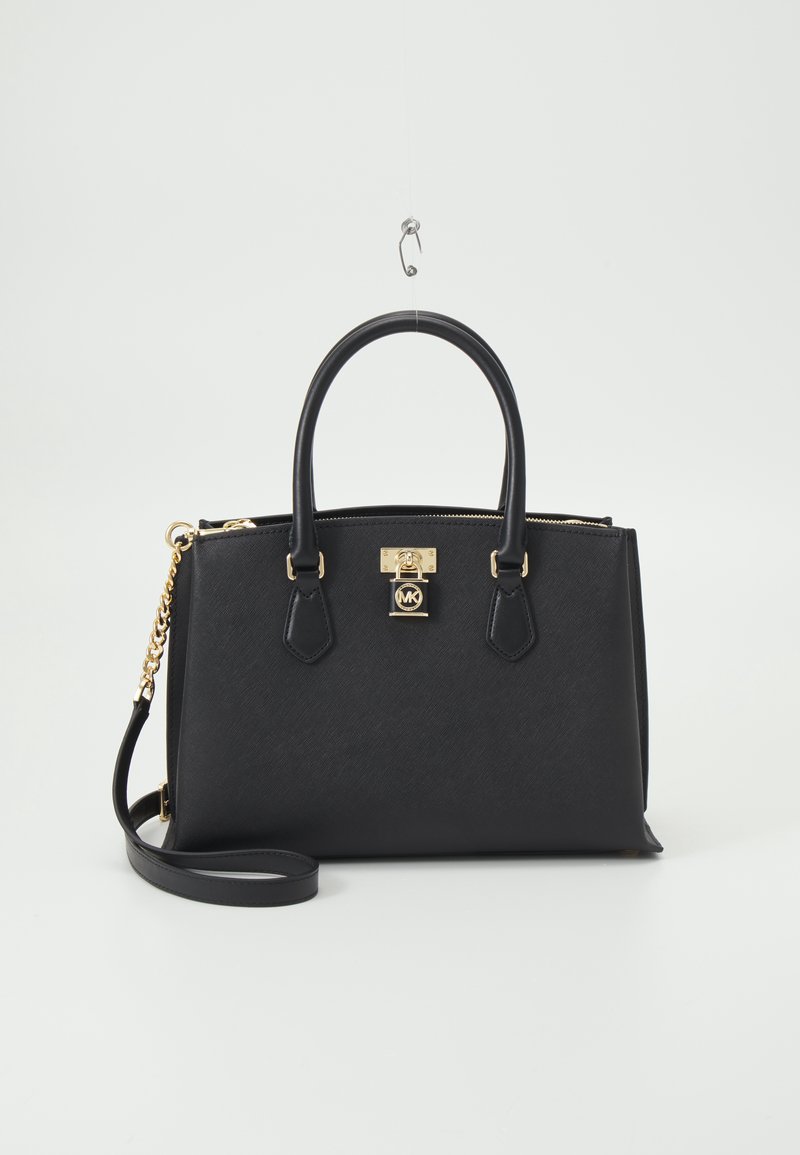 Sac à main en cuir noir avec double poignée, bandoulière chaîne dorée et détail cadenas doré avec logo MK, sur fond blanc.