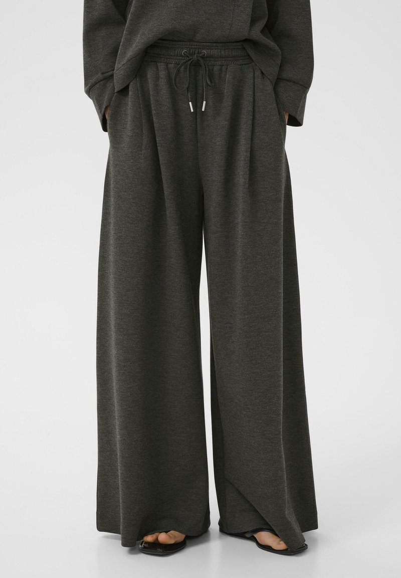 Pantalons de survêtement large gris foncé en tissu doux, avec une taille élastique à cordon et des poches latérales.