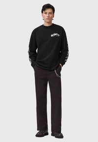 Camiseta negra de manga larga con diseños gráficos en el pecho y las mangas, combinada con pantalones oscuros que incluyen un detalle de cadena en la cintura.