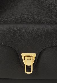 Black textured leather handbag with a gold geometric clasp. Features smooth edges and subtle stitching detail.