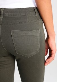 Olivgrön denimjeans med en bakficka med subtila sömnadsdetaljer och en medelhög midja, tillverkade av elastisk, strukturerad tyg.