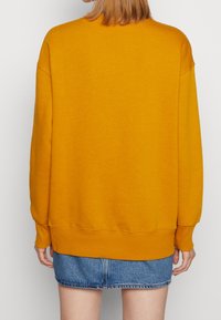 Sweatshirt jaune avec une coupe décontractée, épaules baissées, bords côtelés aux poignets et à l'ourlet, associé à une jupe mini en jean. Texture de tissu lisse et doux.