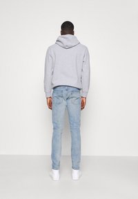 Grå huva sweatshirt som kombineras med ljusblå jeans, med en smal passform. Anmärkningsvärda detaljer inkluderar standardfickor och enkla vita sneakers.