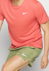 Nike athletic shirt in coral, short-sleeved, paired with olive green athletic shorts. Both feature a white Nike logo.