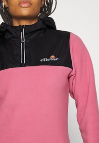 Pullover in felpa con design a blocchi di colore nero e rosa. Presenta un colletto alto, zip frontale e dettaglio logo sul petto. Texture liscia.