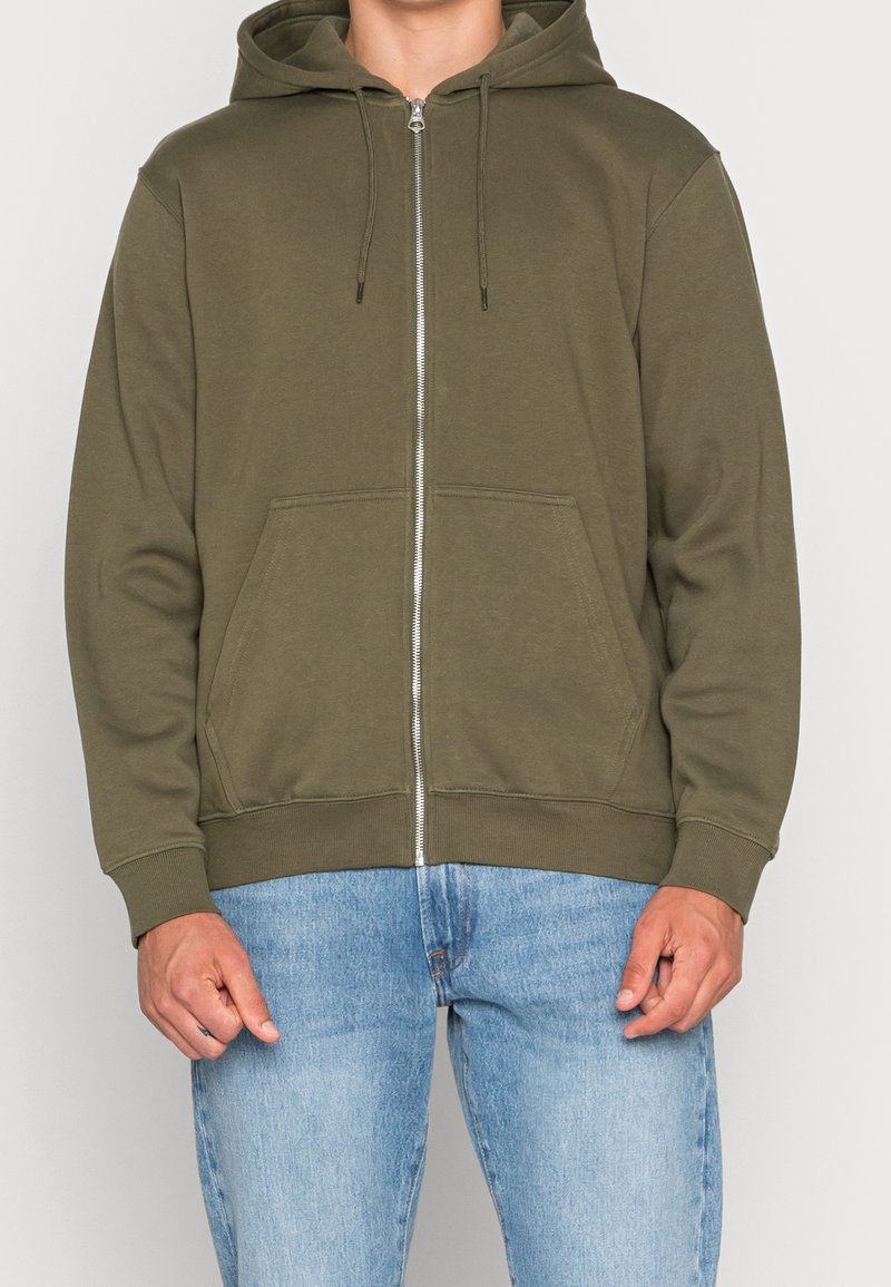 Olivgrüner Reißverschluss-Hoodie mit einer Fronttasche, Kordelzugkapuze, gerippten Bündchen und Saum. Weiches Baumwollmischgewebe mit glatter Textur.