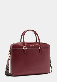 Burgundy læderhandtaske med guldfarvede detaljer, dobbelte top hanke og en aftagelig skulderrem; glat tekstur med subtil kornstruktur.