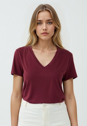 Burgunder V-Ausschnitt T-Shirt aus weichem Stoff mit kurzen Ärmeln, kombiniert mit crema-farbenen Hosen. Einfaches Design ohne sichtbare Muster oder Akzente.