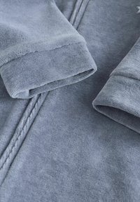 Blød, lyseblå fleece-stof med to rullede ærmer, der fremhæver en glat tekstur og minimale sømdetaljer.