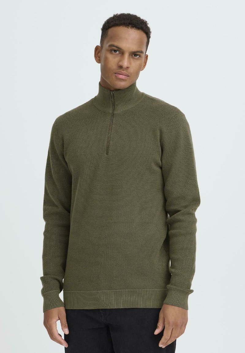 Oliven grønn strikkegenser med høy krage og kvart glidelås-design, med ribbestrikkede mansjetter og fald for en tettsittende look.