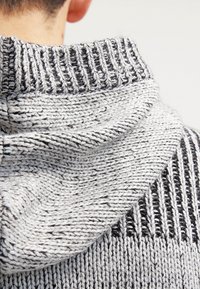 Stickad tröja med ett grått och svart randigt mönster. Har en ribbad huva och krage med en mjuk, texturerad yta.