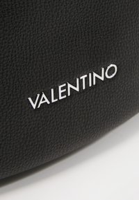 Svart texturerad läderväska med en silverfärgad "VALENTINO"-logotyp präglad på ytan. Designen är elegant och minimalistisk.