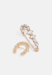 Guldtonet sikkerhedsnål broche med perle og klare krystalkanter, der har et hestesko design og et zigzag mønster på toppen.