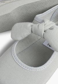 Hellgraue Stoffballerinas mit einer geknoteten Schleife an der Vorderseite. Runde Zehenform und gepolsterte Innensohle, mit weißen Nähten entlang der Kanten.