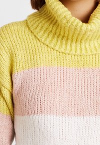 Sweter dziergany z wysokim prążkowanym kołnierzem. Posiada poziome paski w kolorach żółtym, różowym i białym. Miękka tekstura oraz luźny krój.