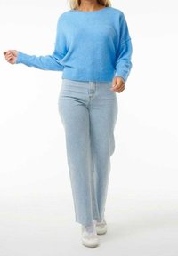 Jasnoniebieski sweter wykonany z miękkiej tkaniny, o luźnym kroju i ściągaczu u dołu. Połączony z jasnymi, wysokim stanem dżinsami i białymi trampkami.