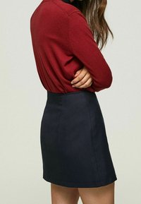 Pull en maille rouge associé à une mini-jupe trapèze bleu marine foncé, mettant en valeur une texture lisse et un design simple sans ornements supplémentaires.