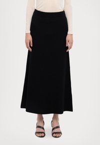 Sort ribbet maxi skørt med bred talje og lige silhuet. Sammen med sorte strop sandaler. Enkel baggrund.