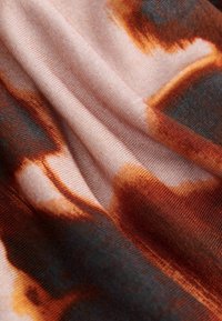 Audinys su minkšta tekstūra šviesiai rožinėmis, oranžinėmis ir tamsiai pilkomis spalvomis, turintis išsiliejusį abstraktų raštą visame paviršiuje.