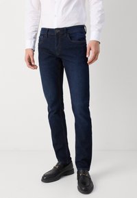 Jeans in denim blu scuro con vestibilità slim, dotati di tasche anteriori e posteriori, cuciture visibili e chiusura tradizionale con bottone e cerniera.
