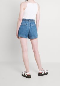 Shorts de mezclilla con cinturilla elástica, color azul claro y un ajuste holgado. Presentan bolsillos traseros y un dobladillo deshilachado. Combinados con sandalias blancas.