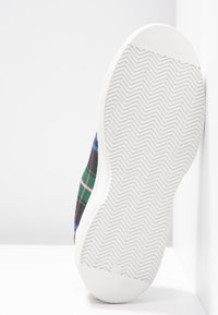 Teniska z kostkované plátna se vzorem v zelené, černé a modré barvě. Bílá gumová podešev s rybí kostí pro lepší přilnavost. Texturovaný svršek.