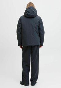 Zwarte pufferjas met capuchon, met een strak ontwerp en een gladde textuur. Gecombineerd met donkere, wijde broekspijpen en platte schoenen.