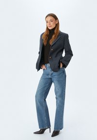 Blazer de rayas azul marino con botones marrones, cuello alto negro y jeans rectos de color azul claro. Modelo con tacones de punta negra.