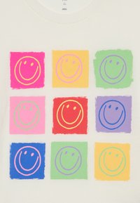 Weißes T-Shirt mit einem Gitter aus neun bunten Quadraten, von denen jedes ein einfaches Smiley-Gesicht in verschiedenen Farben hat: pink, gelb, grün, rot und blau.