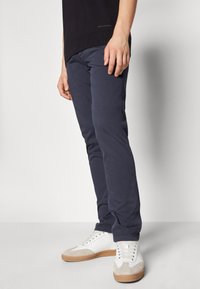 Pantaloni in cotone blu navy con vestibilità slim, abbinati a sneakers bianche con un accento beige e una suola testurizzata.