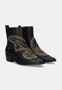 Botas de tobillo negras de cuero con detalles de tachuelas doradas, punteras afiladas, tacones planos y costuras decorativas en los laterales.