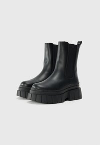 Black leather ankle boots with elastic side panels, chunky platform sole, and a textured rubber bottom. Minimalist design with pull tab.