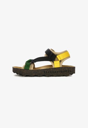 Adjustable sandal featuring a beige upper, black and green straps, and yellow accents. Textured sole with a wave pattern and logo.