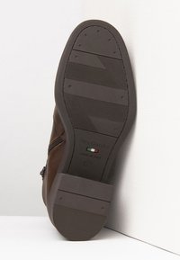 Zapato de cuero marrón con suela de goma texturada. Presenta un cierre lateral y acentos de costura. Marcado con el logo "NeroGiardini" y la bandera italiana.