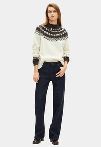 Πλεκτό λευκό πουλόβερ με καφέ λεπτομέρειες και γεωμετρικό σχέδιο, συνδυασμένο με σκούρα μπλε τζιν με φαρδιά μπατζάκια. Ομαλή υφή, άνετη εφαρμογή.