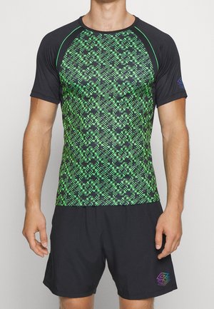 Mann trägt ein kurzärmeliges Sportshirt mit schwarzem und grünem Muster und einfache schwarze Shorts vor weißem Hintergrund.