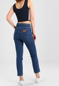 Jeans a vita alta in denim blu medio con una gamba dritta, caratterizzati da una leggera scoloritura, una patch in pelle sul retro e orli risvoltati.