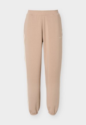 Béžové tepláky s elastickým pásom, ukončené lemami na členkoch a jemnými bočnými pásmi, s malým logom "GUESS" na hornej časti stehna.