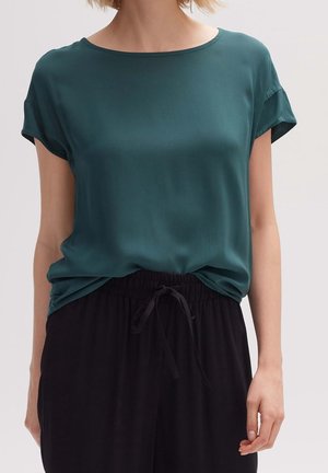 Turquoise blouse met korte mouwen van lichtgewicht stof met een ronde halslijn. Gecombineerd met zwarte, loszittende broek met een elastische tailleband.