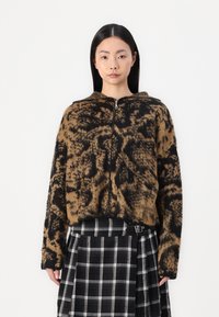 Sudadera con capucha y cremallera en estampado animal marrón y negro, que presenta un tejido de punto texturizado. Combinada con una falda de cuadros en blanco y negro.