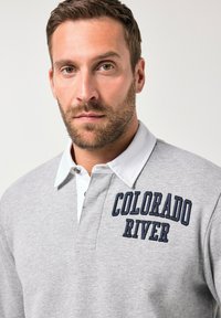 Polo grigio realizzato in cotone, con colletto bianco e testo ricamato "COLORADO RIVER" in blu navy. Texture morbida e design classico.