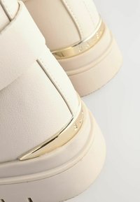 Witte neplederen hoge sneakers met een metalen gouden accent rondom de hak en gestikte details. Textuur oppervlak met een dikke zool.
