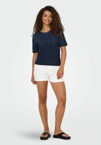 Navy gebreid T-shirt met korte mouwen en ribbelstructuur, gecombineerd met witte opgerolde shorts en zwarte teenslippers. Eenvoudig ontwerp, casual pasvorm.