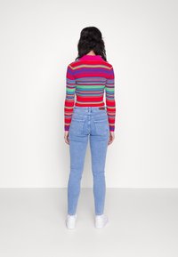 Přiléhavý barevný pruhovaný crop top s dlouhými rukávy; v kombinaci se světlými modrými džíny s vysokým pasem a bílými teniskami.