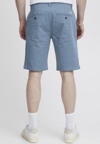 Light blue shorts with a textured pattern, featuring back pockets and a straight leg cut, worn with white socks and sneakers.
