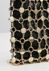 Bolso de cuero negro cubierto con una red geométrica dorada de cadenas que presenta anillos interconectados y discos circulares planos.
