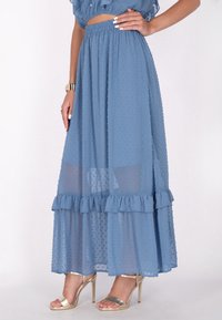 Maxi gonna blu chiaro con texture a pois, orlo arricciato e sovrapposizione trasparente. Indossata con sandali metallici con cinturini.