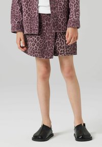 Denim jakna s leopardjim uzorkom u mauve tonovima, uparena s odgovarajućom suknjom, obje s podrezanim rubovima, nošena s crnim klokanicama.