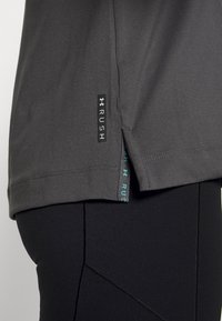 Camisa deportiva de manga corta gris con aberturas laterales y etiqueta con el logo "RUSH", combinada con pantalones ajustados negros con un diseño texturizado.